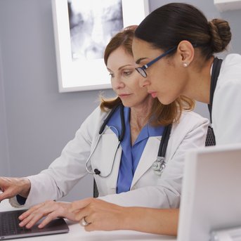 Zwei Ärztinnen betrachten gemeinsam einen Laptop in einem modernen Büro, während sie Informationen überprüfen.