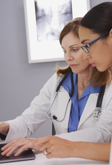 Zwei Ärztinnen betrachten gemeinsam einen Laptop in einem modernen Büro, während sie Informationen überprüfen.