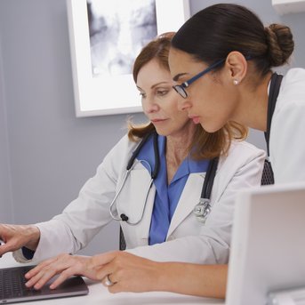 Two female doctors are looking at a laptop together in a modern office as they review information.