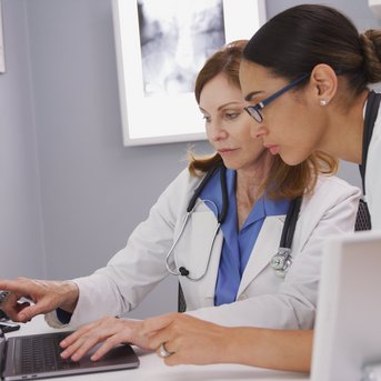 Two female doctors are looking at a laptop together in a modern office as they review information.