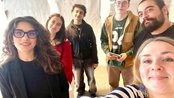 Sechs Personen posieren für ein Gruppenfoto in einem hellen Raum, mit Zeichnungen im Hintergrund. Alle lächeln in die Kamera.