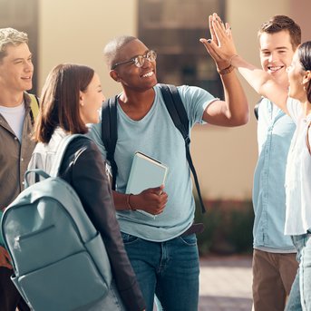Sechs junge Erwachsene stehen zusammen, lächeln und geben sich gegenseitig High-Fives, während sie Rucksäcke und Bücher halten.