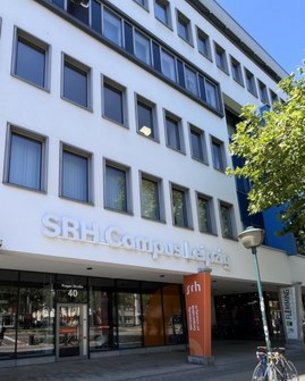 Fassade des SRH Campus Leipzig mit großen Fenstern und einem Eingangsbereich. Ein Fahrrad steht vor dem Gebäude.