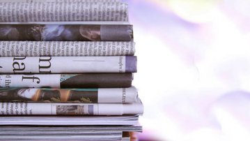 Gestapelte Zeitungen und Magazine in verschiedenen Formaten, die auf einem Tisch liegen.