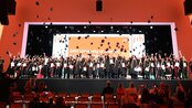 Graduates of SRH University Heidelberg celebrate their graduation by throwing their caps in the air while standing on stage.