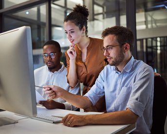 Drei Personen arbeiten gemeinsam an einem Computer, während sie Informationen auf dem Bildschirm überprüfen und diskutieren.