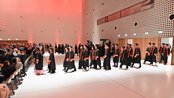 Graduates in academic robes walk through a festive event hall during a graduation ceremony.
