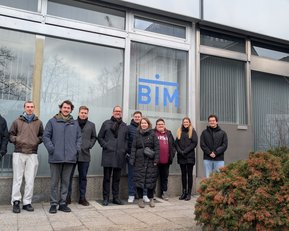 Eine Gruppe von acht Personen steht vor einem Gebäude mit dem Logo "BIM". Sie tragen verschiedene Winterkleidung und posieren freundlich.