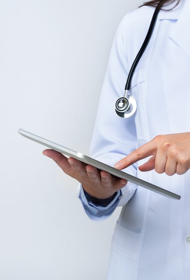 Eine Person in einem weißen Kittel hält ein Tablet und zeigt mit dem Finger darauf. Ein Stethoskop hängt um den Hals.