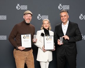 Drei Personen halten Auszeichnungen des German Design Awards 2023 in der Hand, stehen vor einem neutralen Hintergrund.