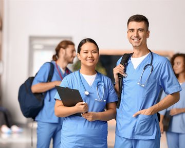 Zwei medizinische Fachkräfte in blauen Uniformen stehen lächelnd zusammen, während im Hintergrund weitere Personen sichtbar sind.