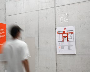 Signpost and floor plan on the ground floor of a building, with information about design studios and labs. A person walks by.