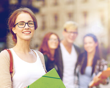 A smiling student with glasses is holding a green notebook, while three other students stand in the background.