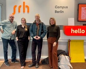 Four people are standing at the reception of the SRH Campus Berlin, with a 'hello' sign in the background.