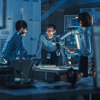 Three people are discussing around a table in a modern laboratory, while a robotic arm is positioned nearby.