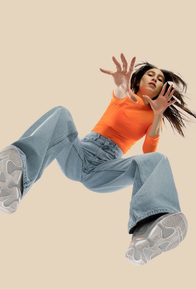 Three women in fashionable outfits jump into the air, each with a different style of clothing and shoes.