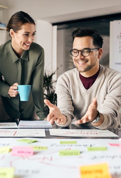 Vier Personen sitzen an einem Tisch, diskutieren und arbeiten an einem Projekt mit Notizen und Diagrammen. Eine Person hält eine Tasse.