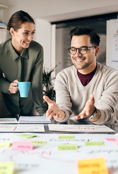Vier Personen sitzen an einem Tisch, diskutieren und arbeiten an einem Projekt mit Notizen und Diagrammen. Eine Person hält eine Tasse.