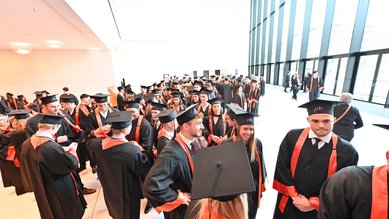 Graduates in academic attire with caps and sashes gather in a modern space, ready for the graduation ceremony.