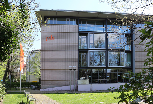 Modern buildings with large windows and the inscription 'srh' on the facade, surrounded by trees and a well-maintained garden.