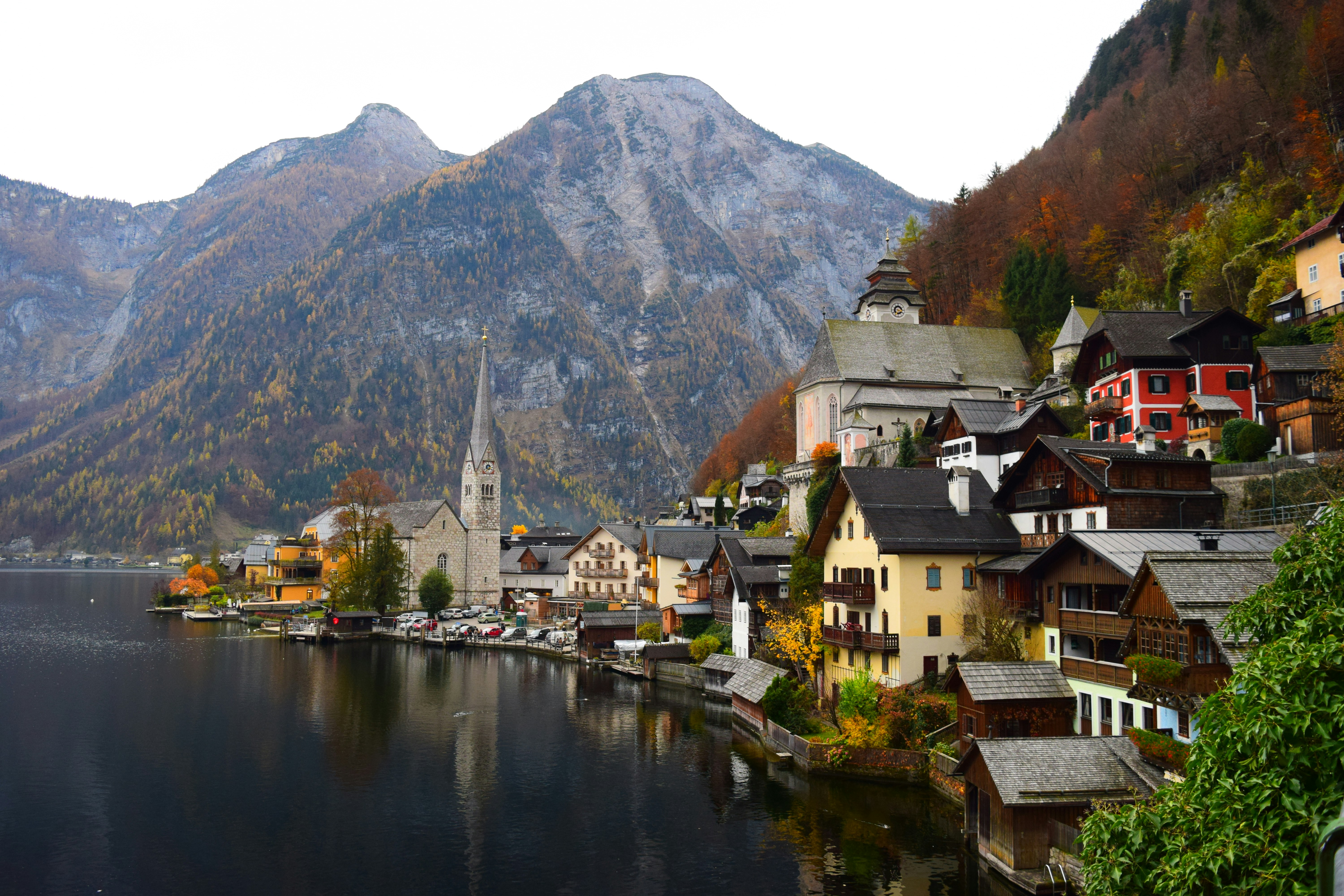 Blick auf das malerische Dorf Hallstatt am See, umgeben von Bergen und herbstlichen Bäumen. Historische Gebäude und eine Kirche sind sichtbar.